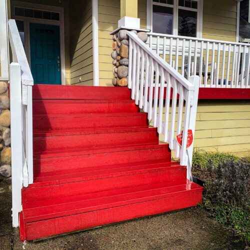 Red staircase leading up to the deck of a yellow house