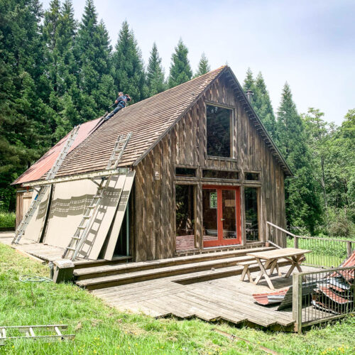 Red roofing being installed on a rustic two story house