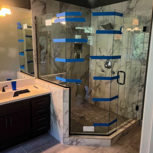 Glass doors on a walk-in shower with marble walls