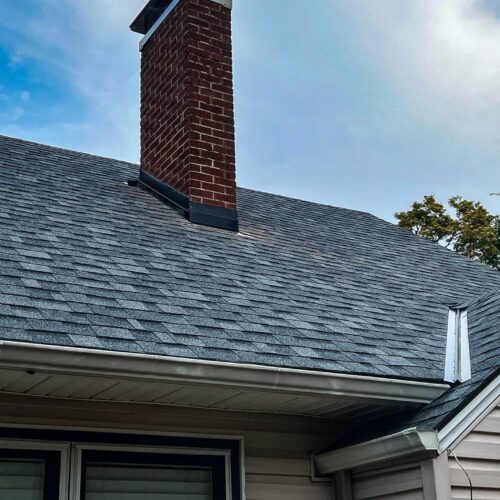 Newly replaced roof shingles around a brick chimney