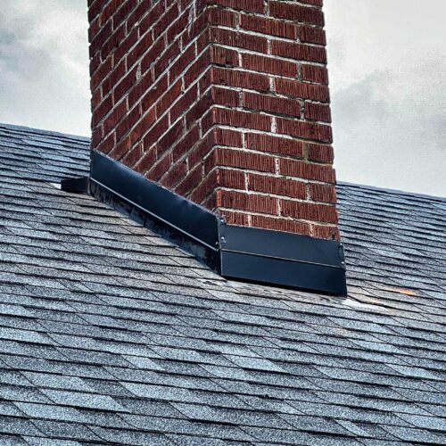 Newly replaced roof shingles around a brick chimney