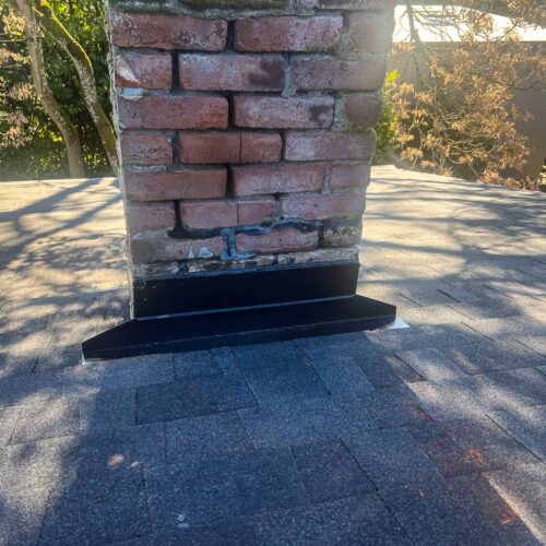 Shadowed old chimney on a shingled roof